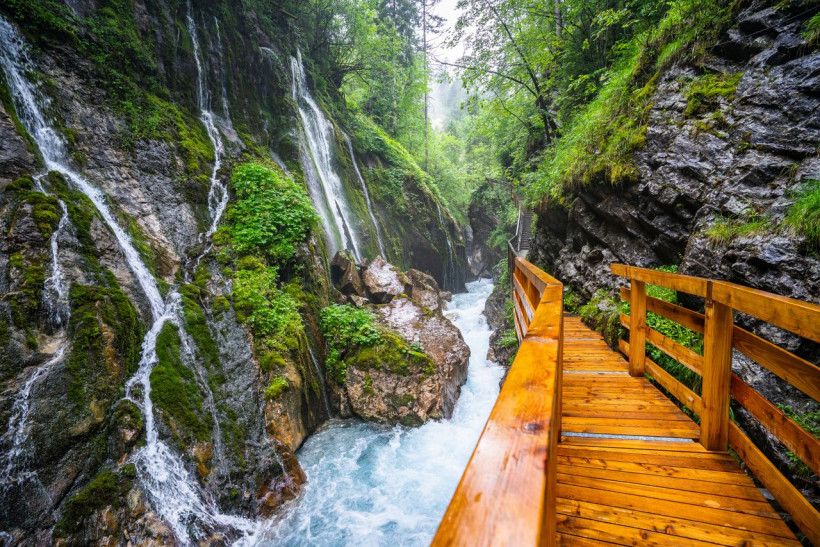 Holzsteg in grüner Klamm mit Wasserfall